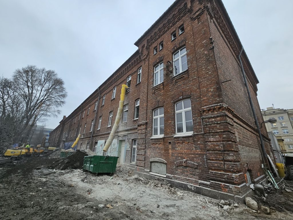 Budynek z zewnątrz podczas przebudowy. Przy ścianie żółta rura do odbioru gruzu.