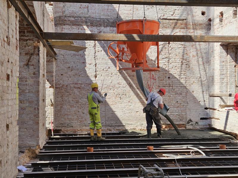 Robotnicy wylewają beton na posadzkę podczas budowy NAC